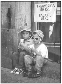 Two Czech children enjoy ice cream, seated on the threshold of a shop advertising two Middle Eastern favorites—shawerma (grilled, skewered meat) and falafil (deep-fried chickpea balls), with prices quoted in Czech currency, the koruny (Kc). Cory Langley